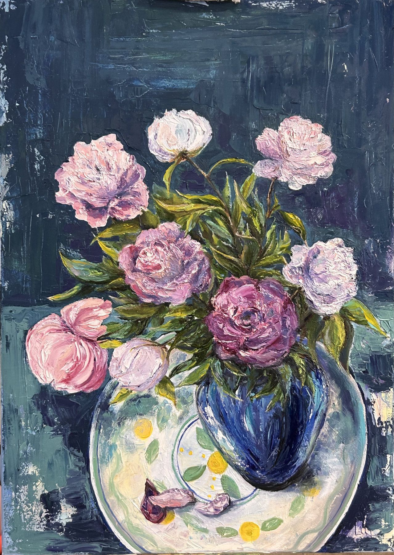 Pink and lilac peonies in a cobalt-blue vase on a painted plate against a dark background.