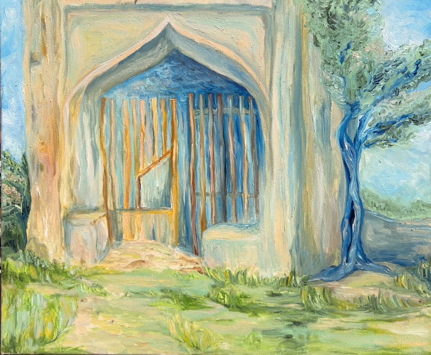 Weathered stone archway with a barred gate and a blue-green tree in sunlit grass.